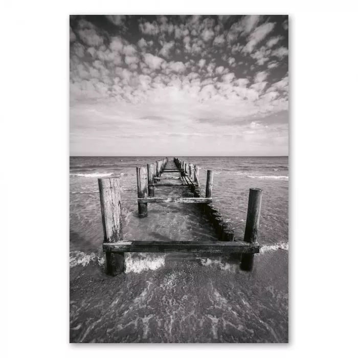 Ein verlassener Holzsteg führt ins Meer, die Wellen brechen am Strand.